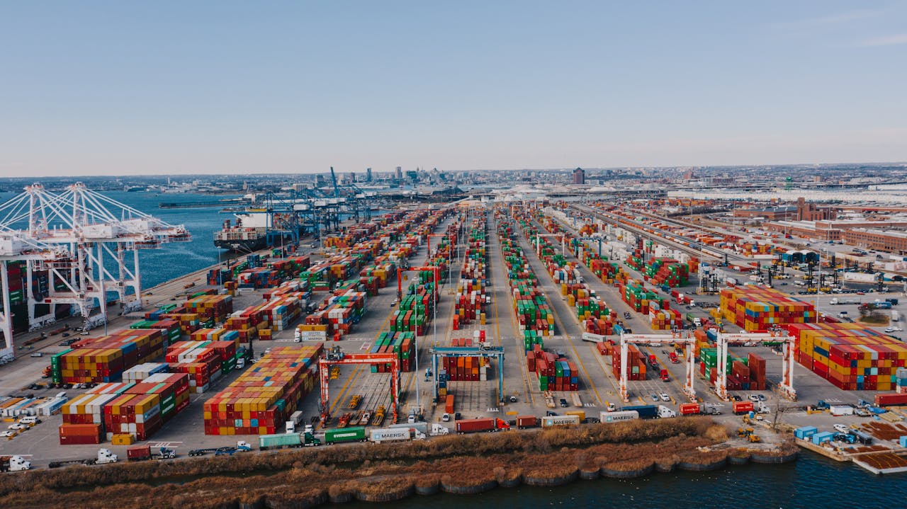 Drone view of river embankment with various bright cargo containers near steel lifting cranes under cloudless sky